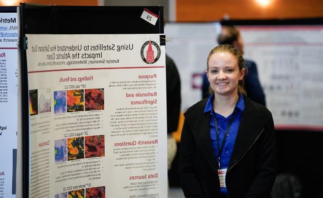 Student in blue top posing in front of poster